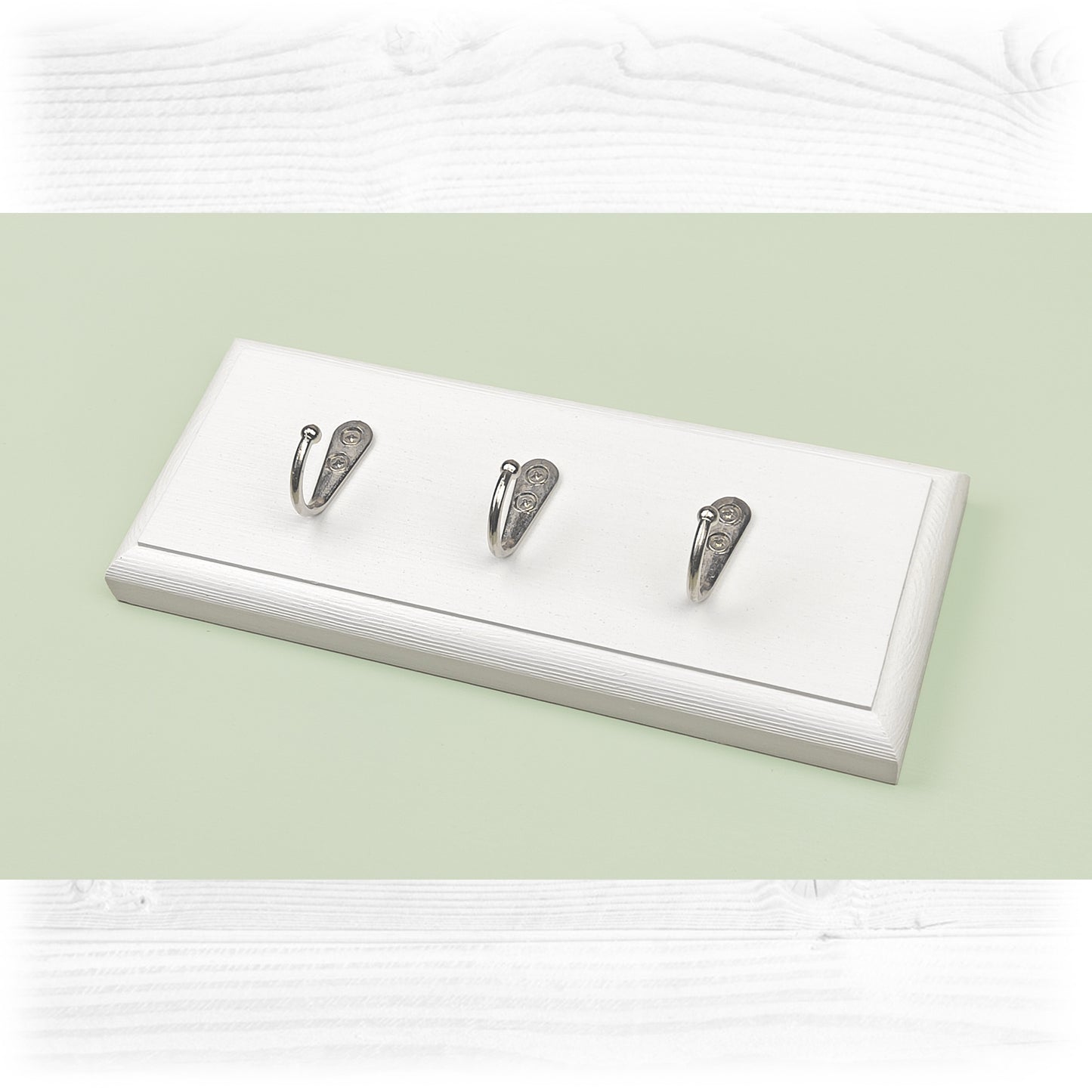 A white wooden floating key rack on a green background with chrome coloured hooks