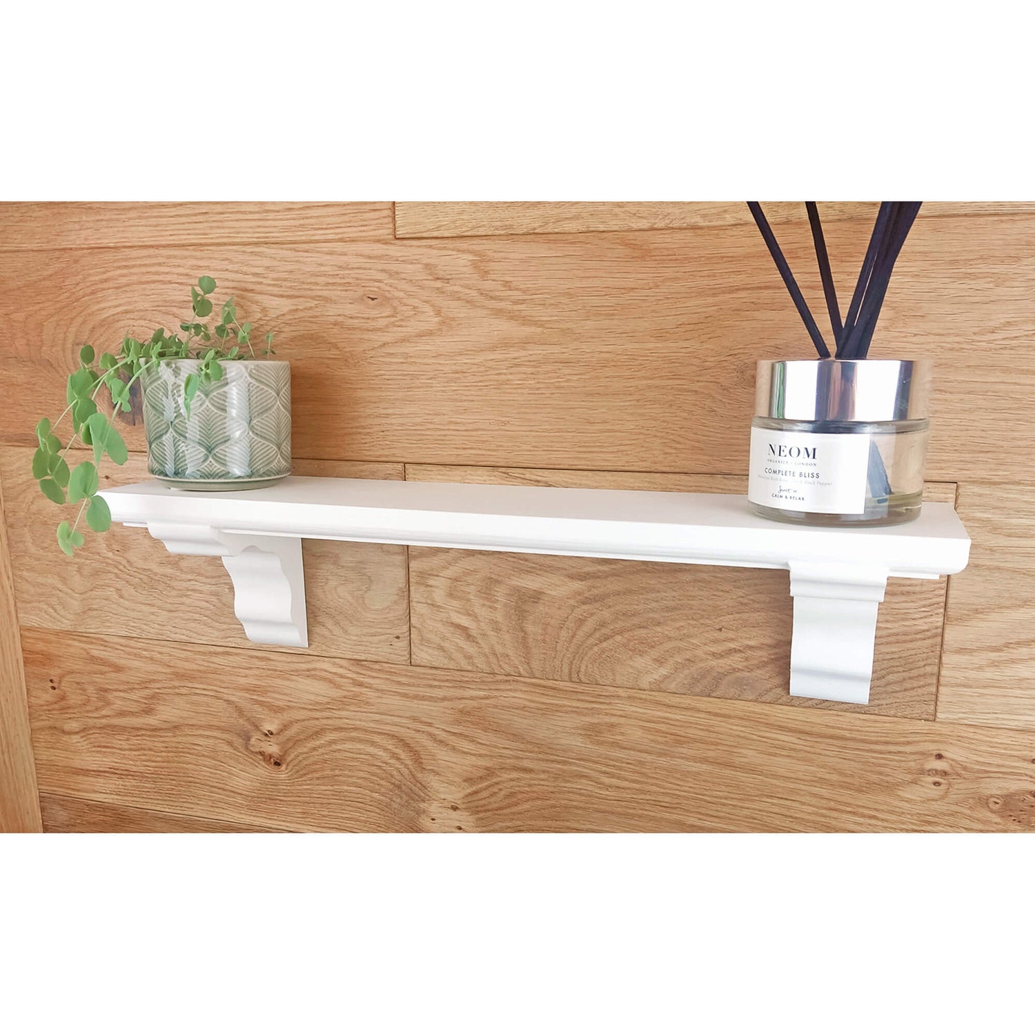 White shelf with a plant and a diffuser on a wooden wall