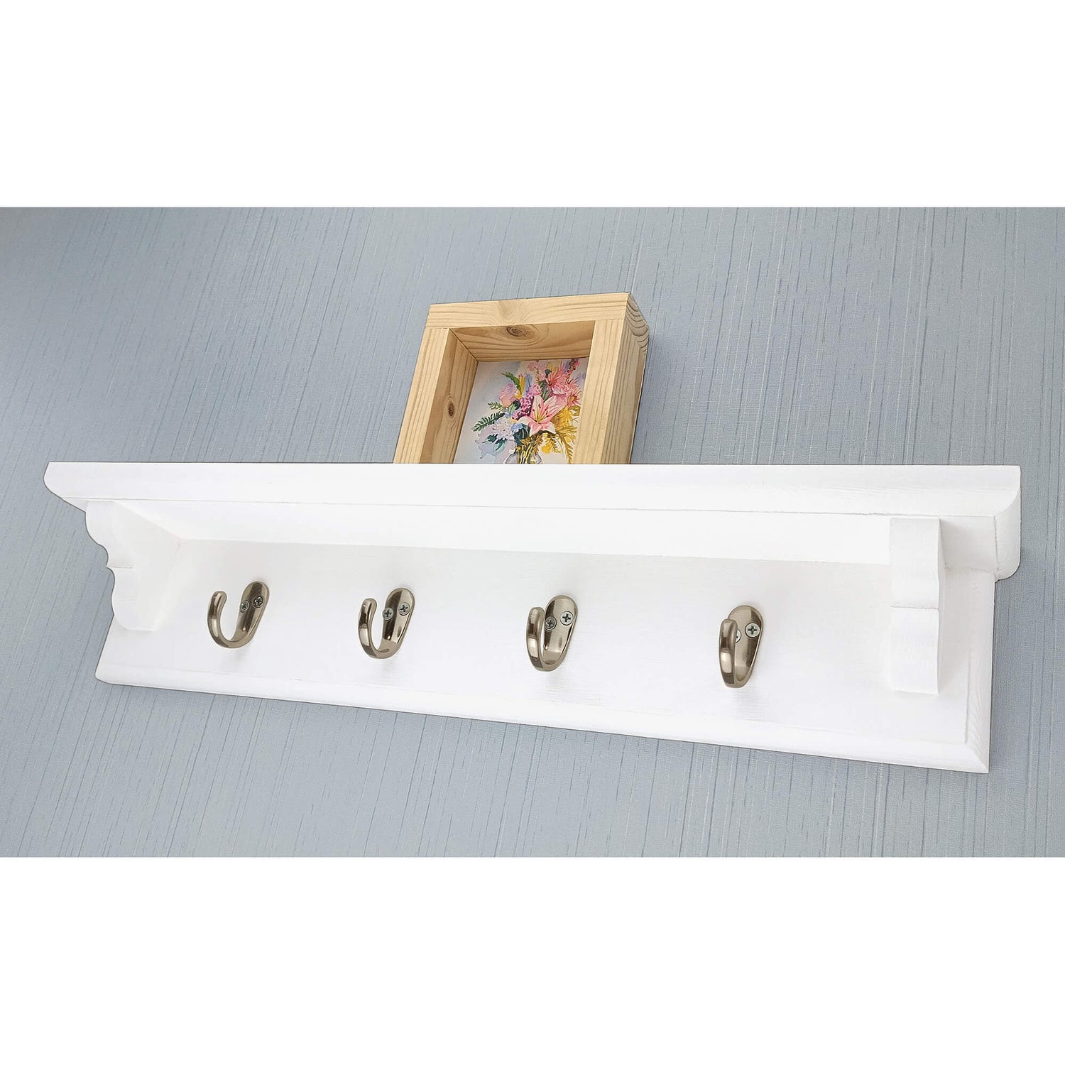 Solid wooden coat rack with metal hooks hung on a blue wallpapered wall with a wooden picture frame sitting on the shelf