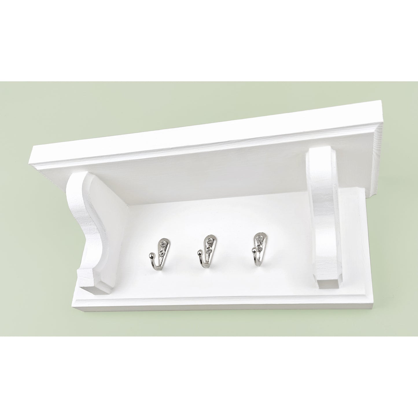 A solid wooden white chalk painted key rack with shelf and chrome key hooks on a green background