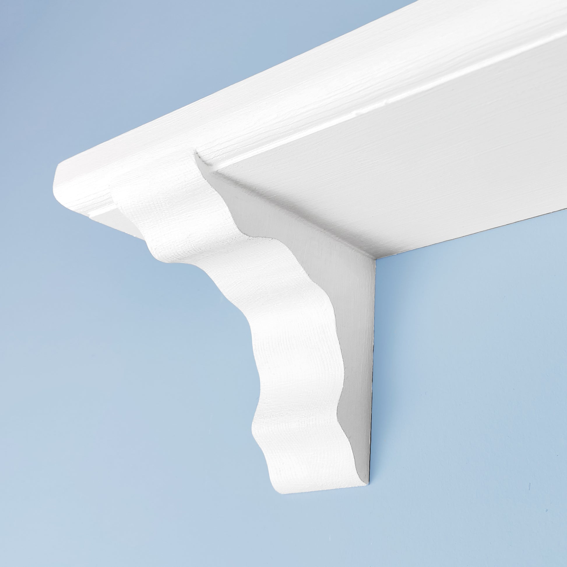 A close up of a corbel on a floating shelf. The shelf is made of solid wood and is painted in a white chalk paint on a blue background