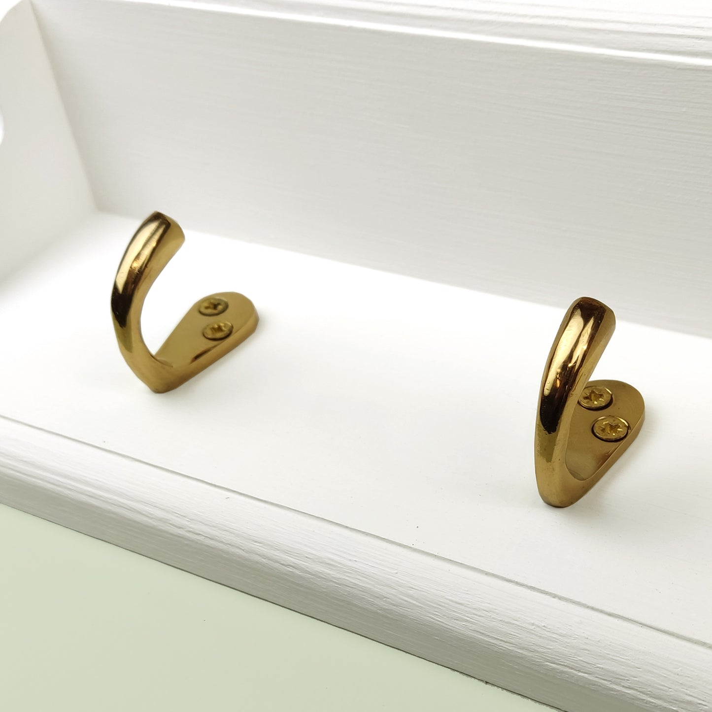 A close up of a solid wooden white chalk painted floating coat rack with brass hooks on a green background