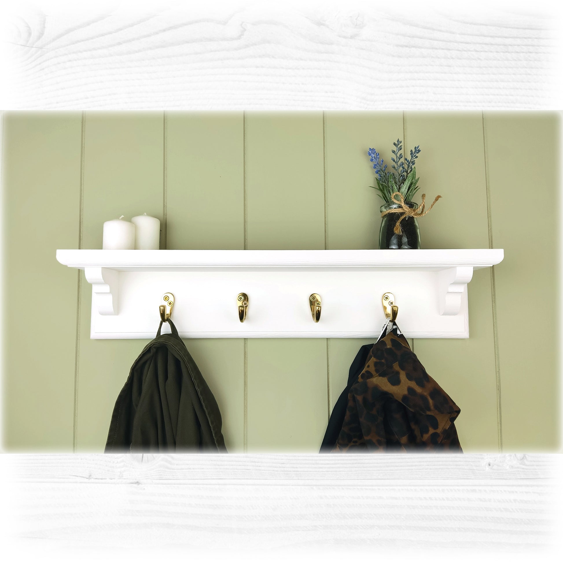 A white wooden floating coat rack with shelf featuring brass coat hooks on a green cladded background