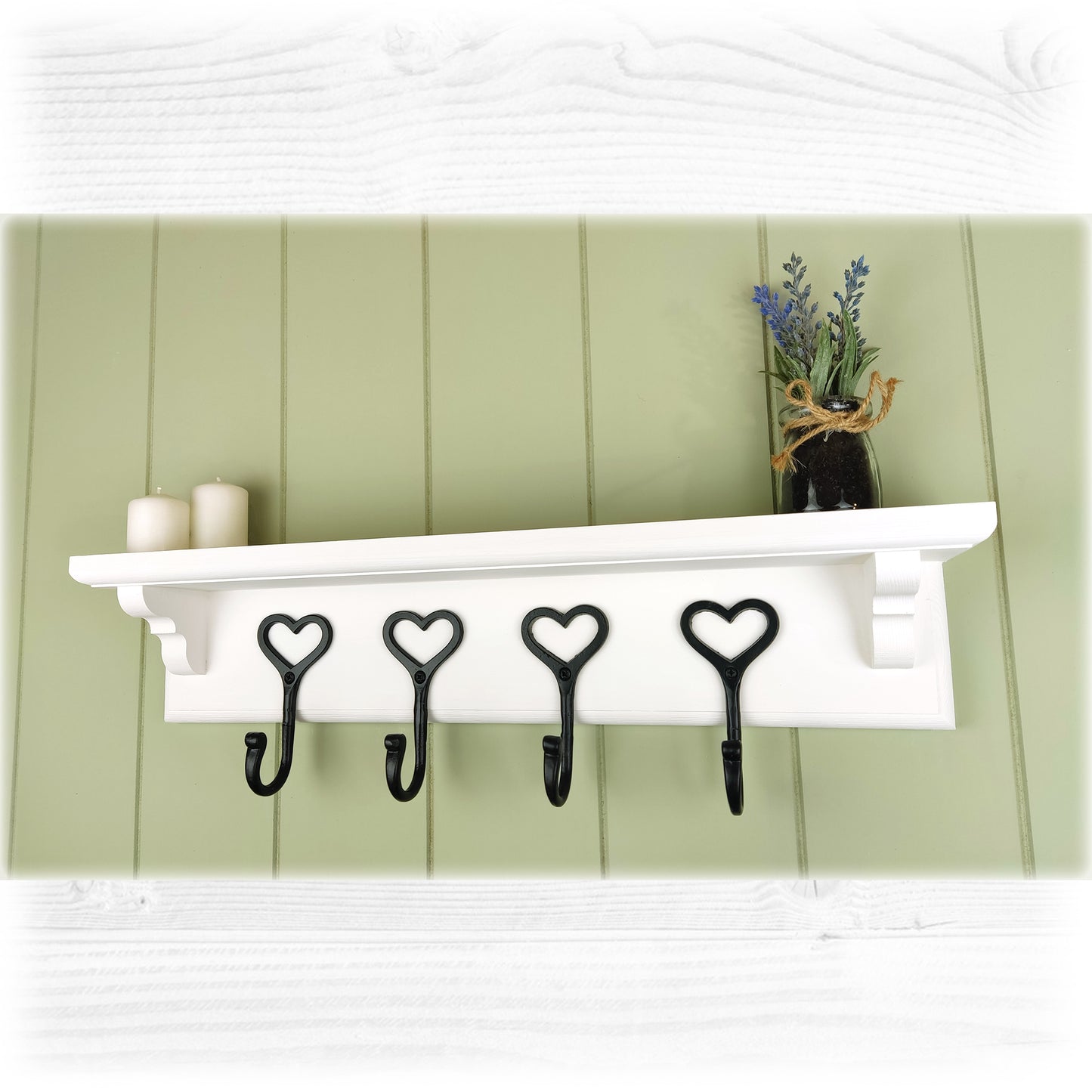 A floating wooden white coat rack with shelf and cast iron black heart shaped coat hooks on a green cladded background