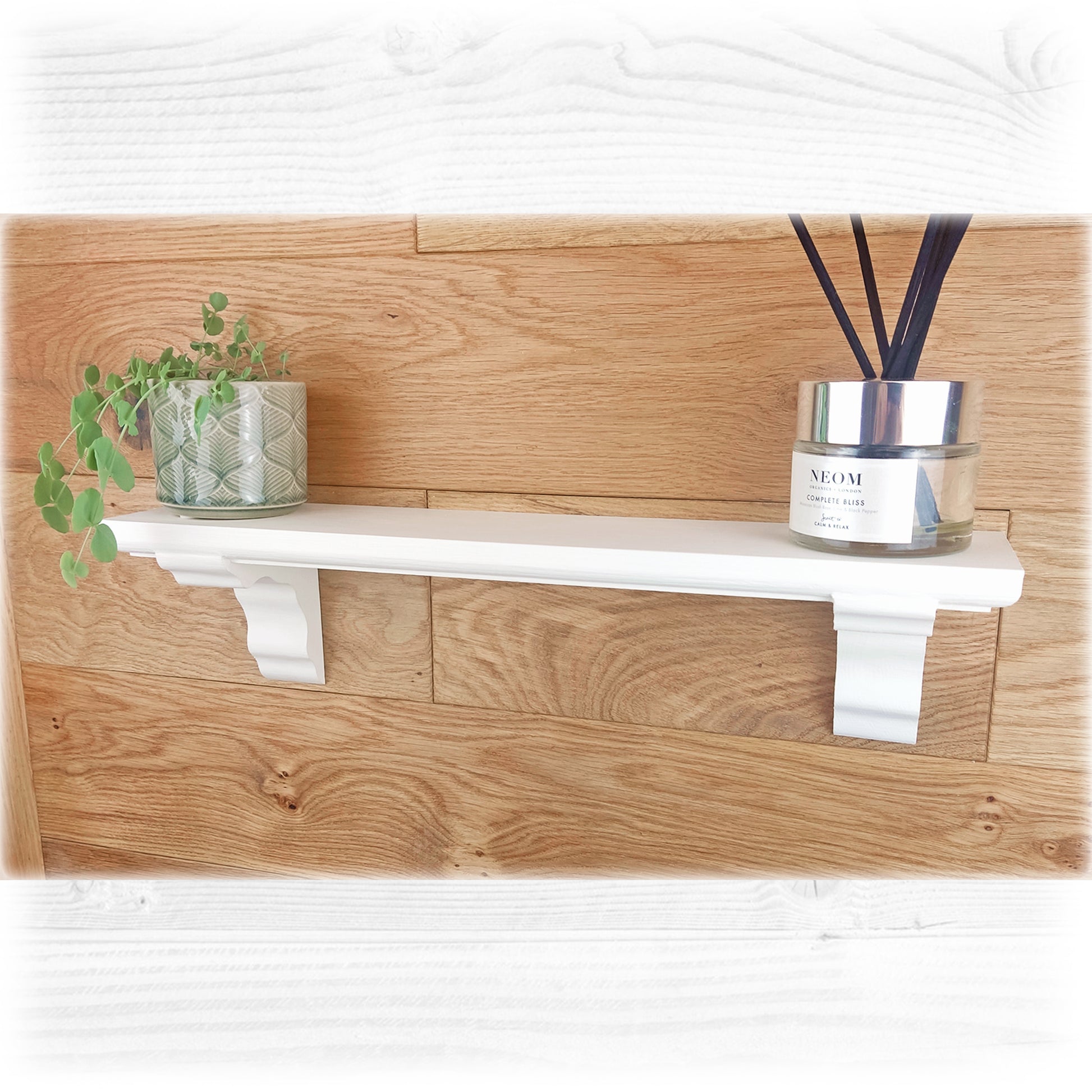 A white floating wooden shelf finished in chalk paint and waxed on an oak wooden background with ornaments sitting on top