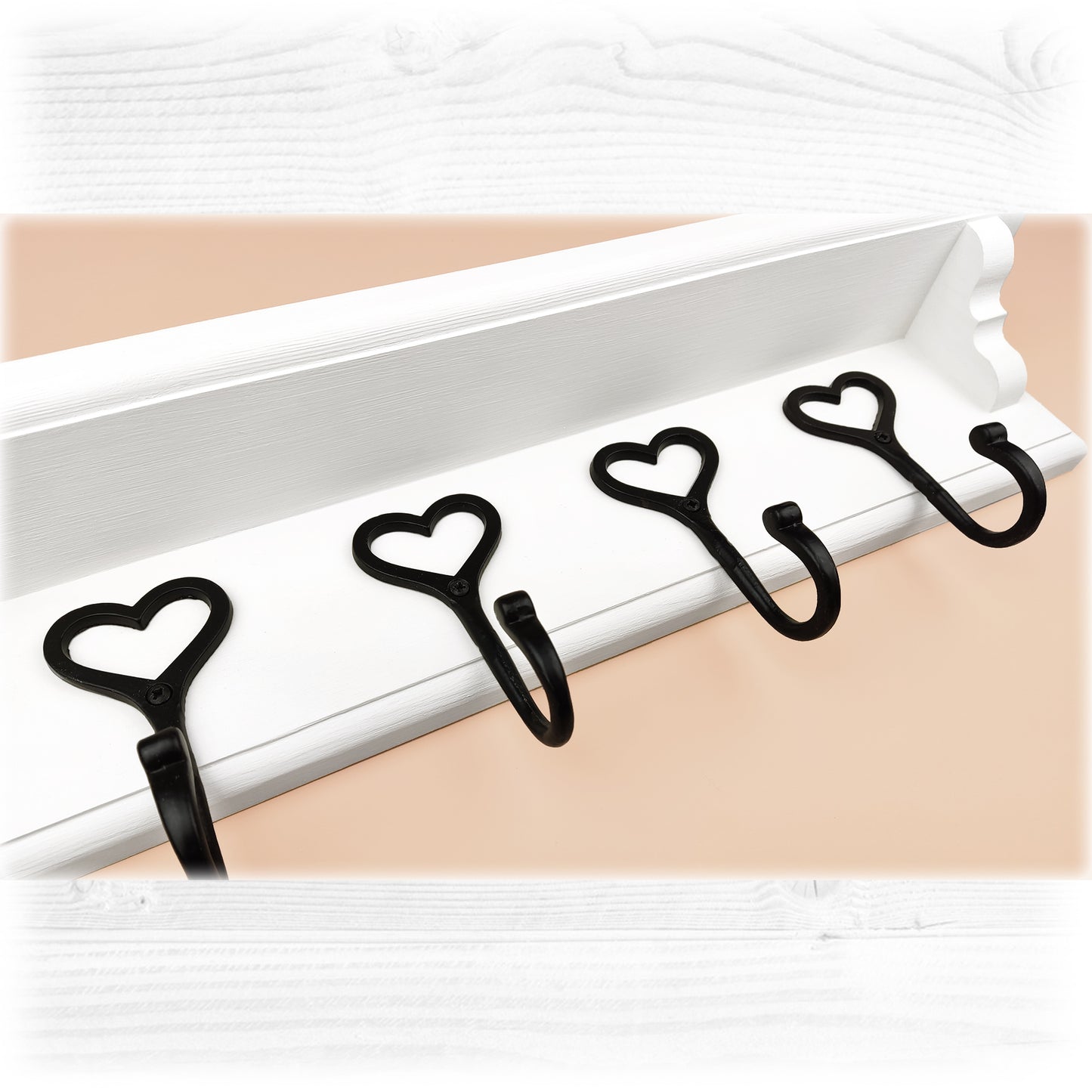 A white floating wooden coat rack with a shelf featuring cast iron black heart shaped hooks