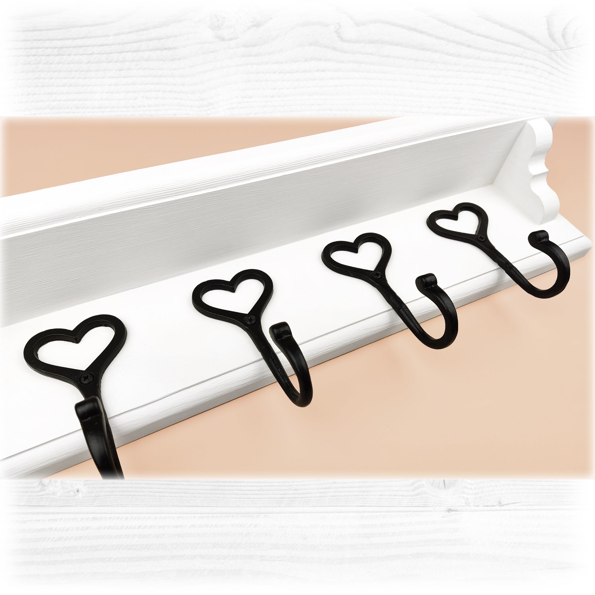 A white floating wooden coat rack with a shelf featuring cast iron black heart shaped hooks