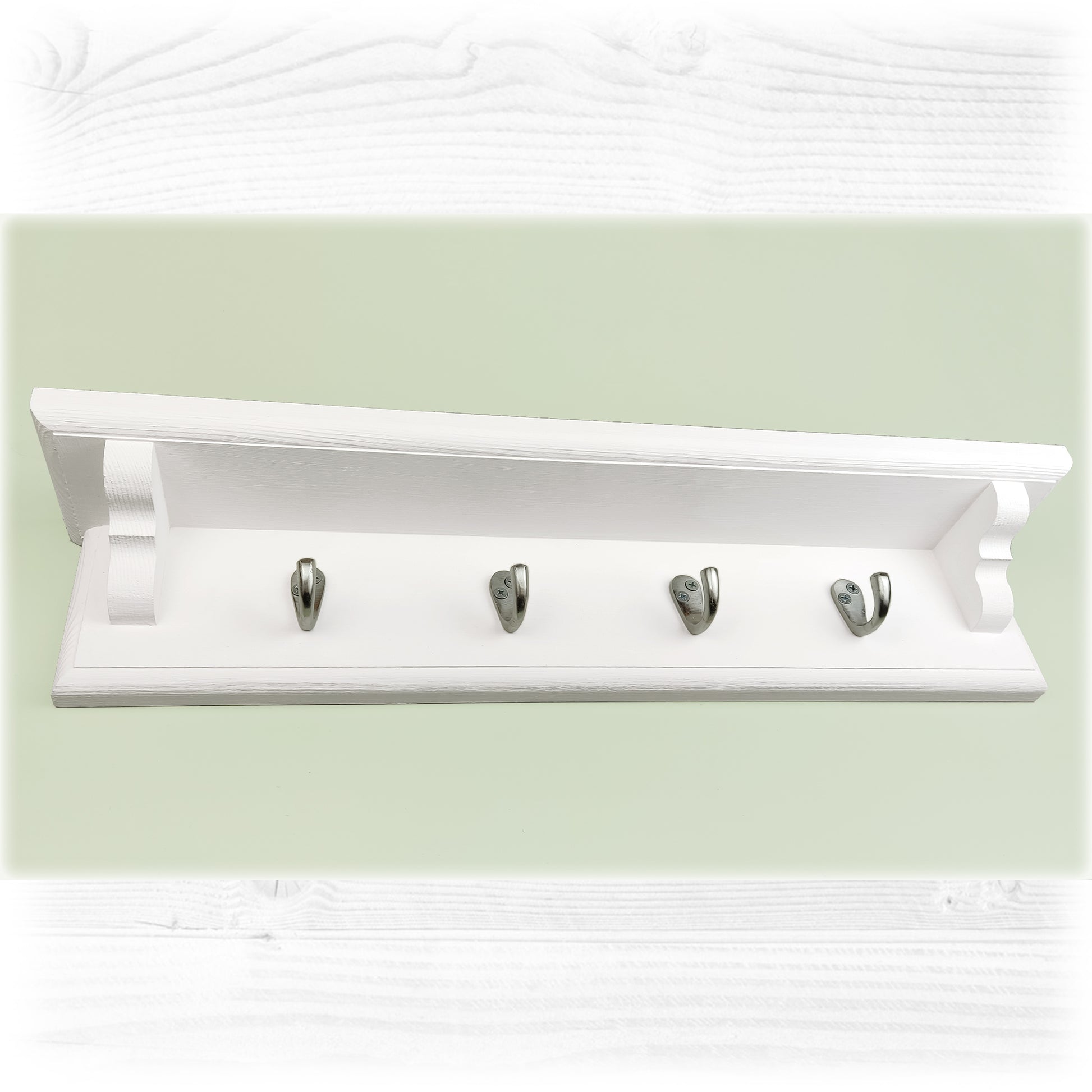 A white floating wooden coat rack with shelf on a green background featuring satin coated coat hooks
