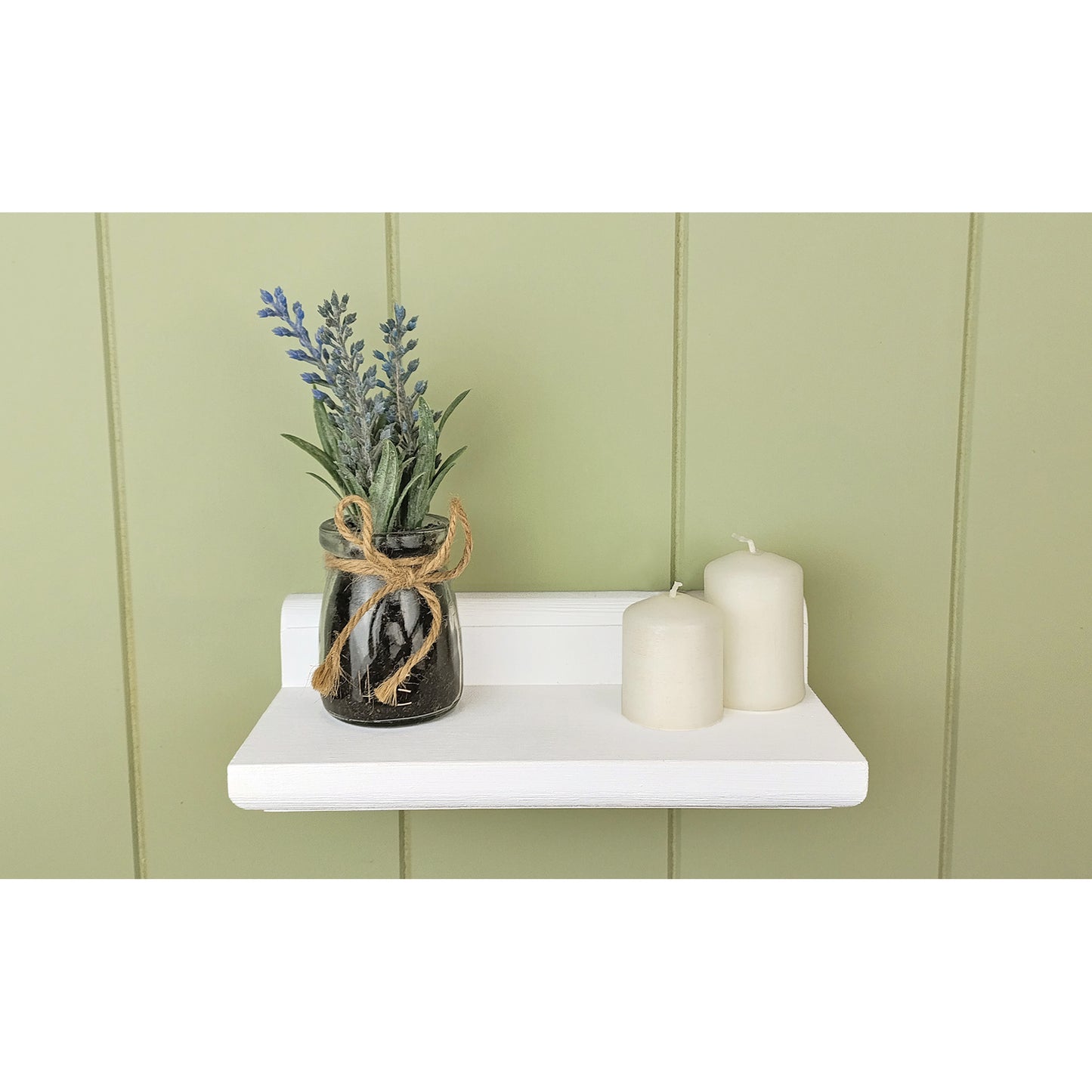 Decorative shelf with a jar of lavender and two candles against a green paneled wall.