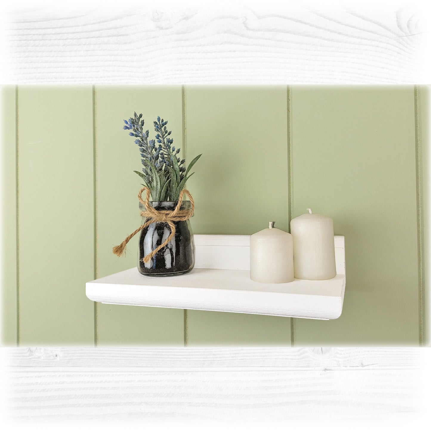 White shelf with a vase of lavender and two candles against a light green wall.