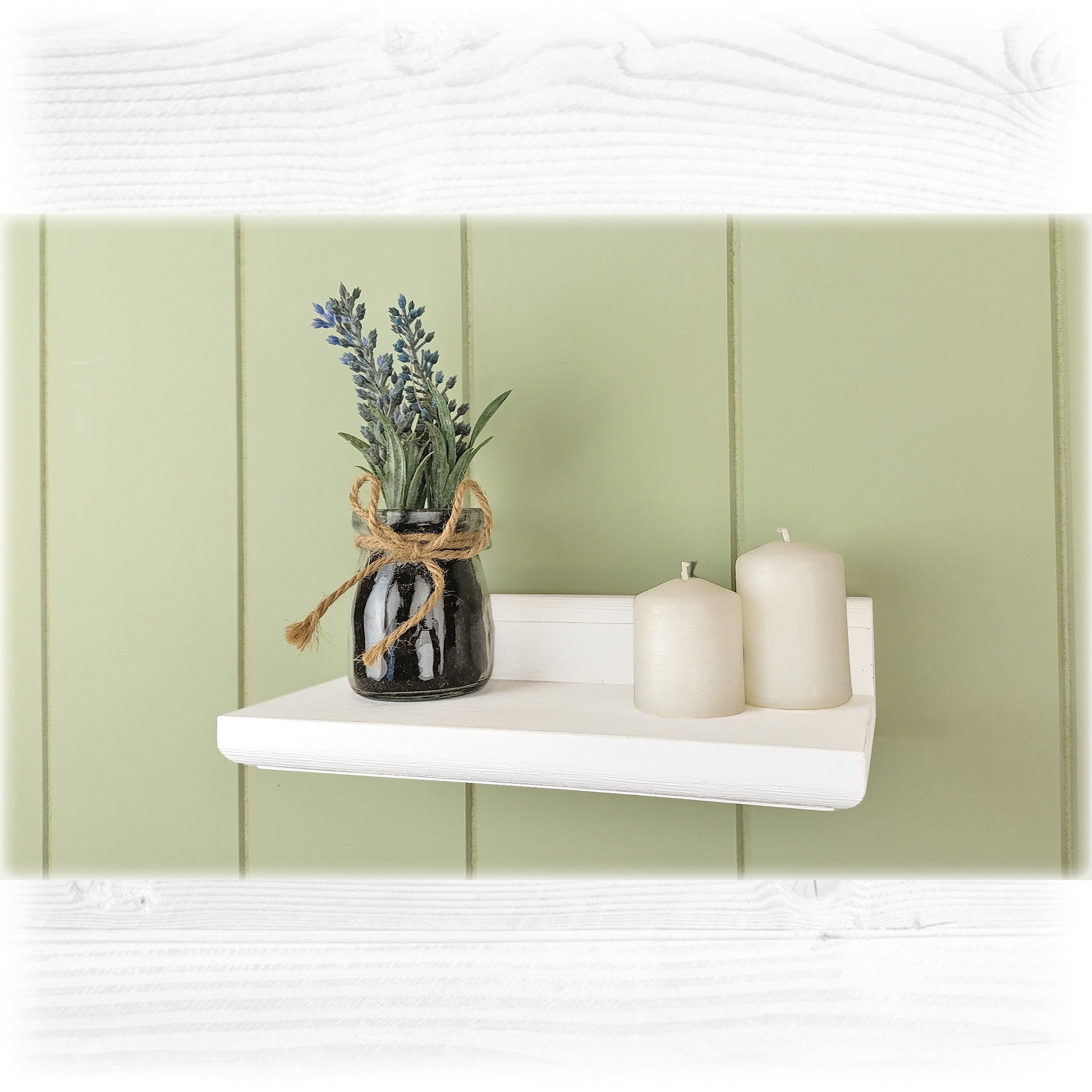 White shelf with a vase of lavender and two candles against a light green wall.