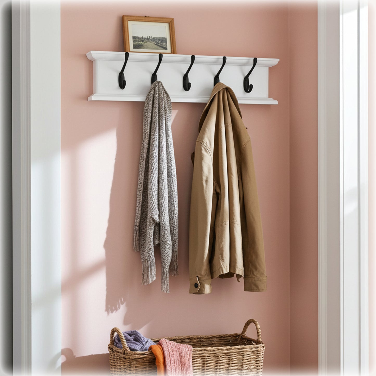 White wall-mounted coat rack with hooks holding two coats against a pink wall.