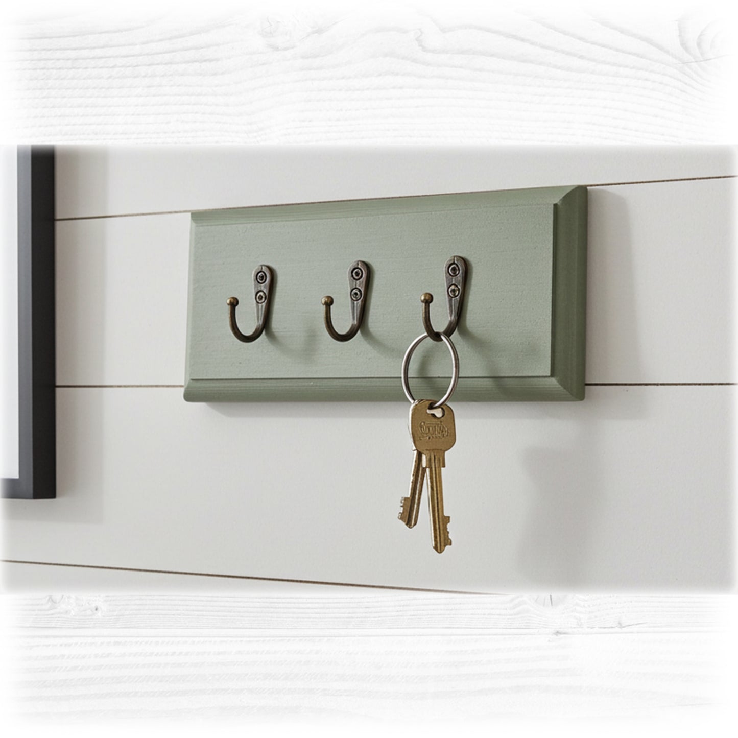 Green wall-mounted key holder with three hooks on a white wooden background