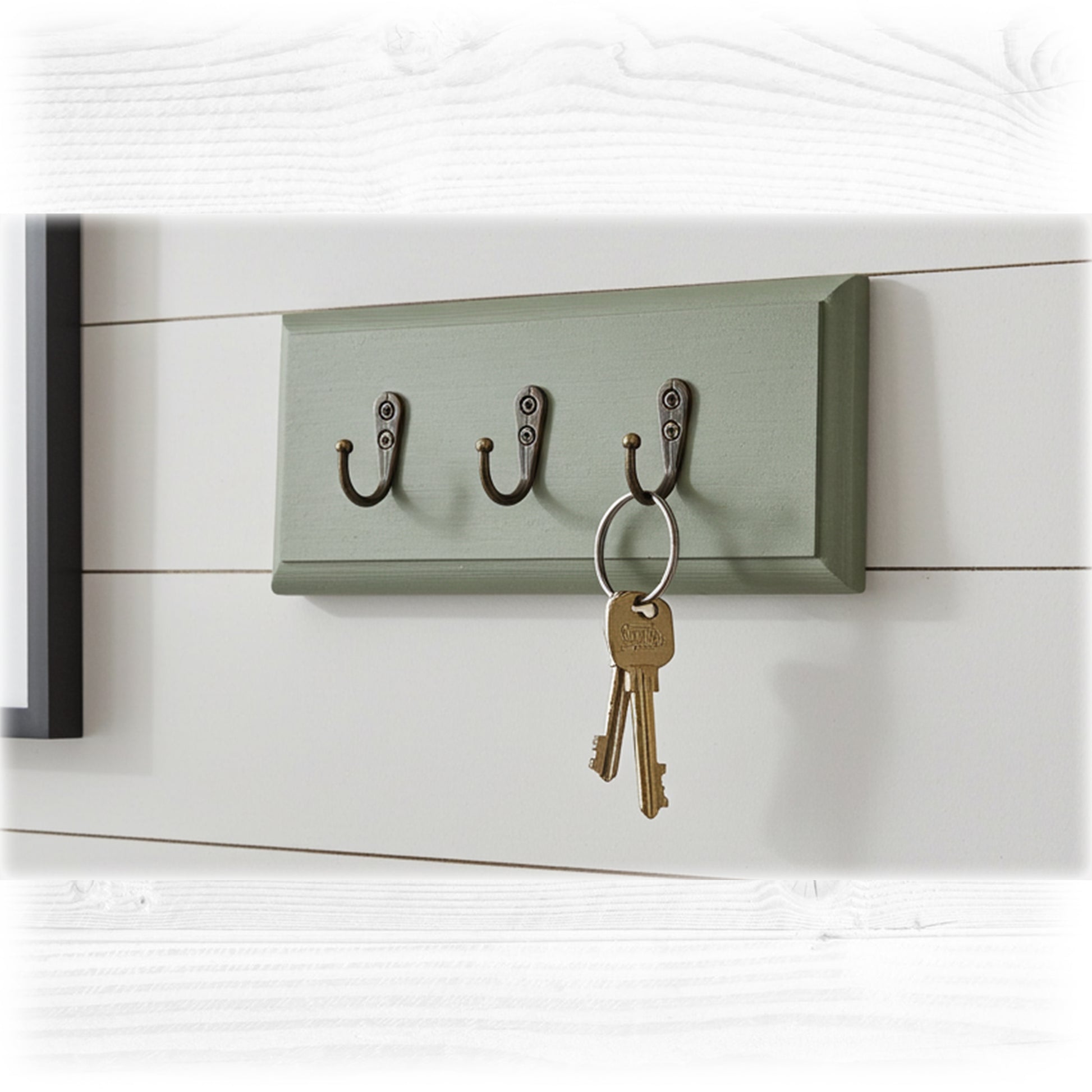 Green wall-mounted key holder with three hooks on a white wooden background
