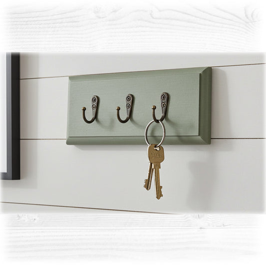 Green wall-mounted key holder with three hooks on a white wooden background