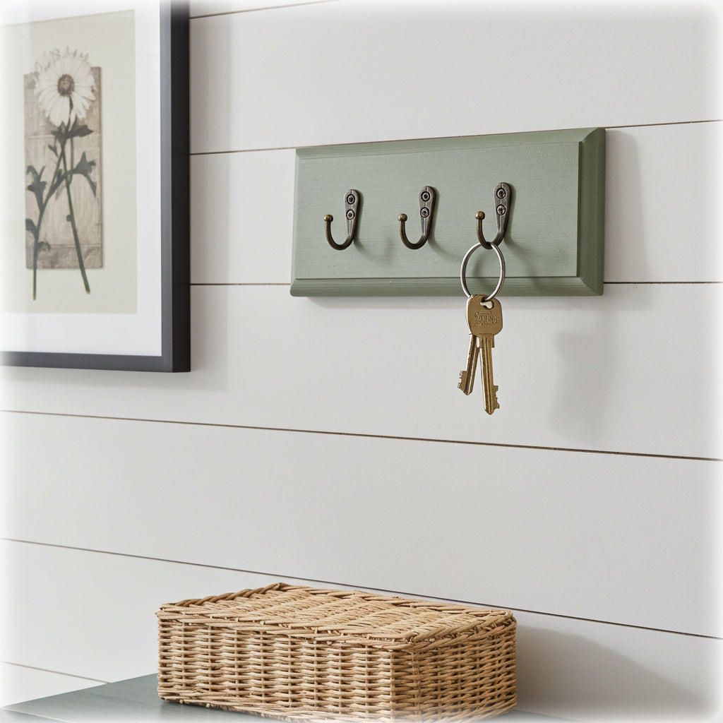 Wall-mounted hook with keys on a white wall with a wicker basket at the bottom.