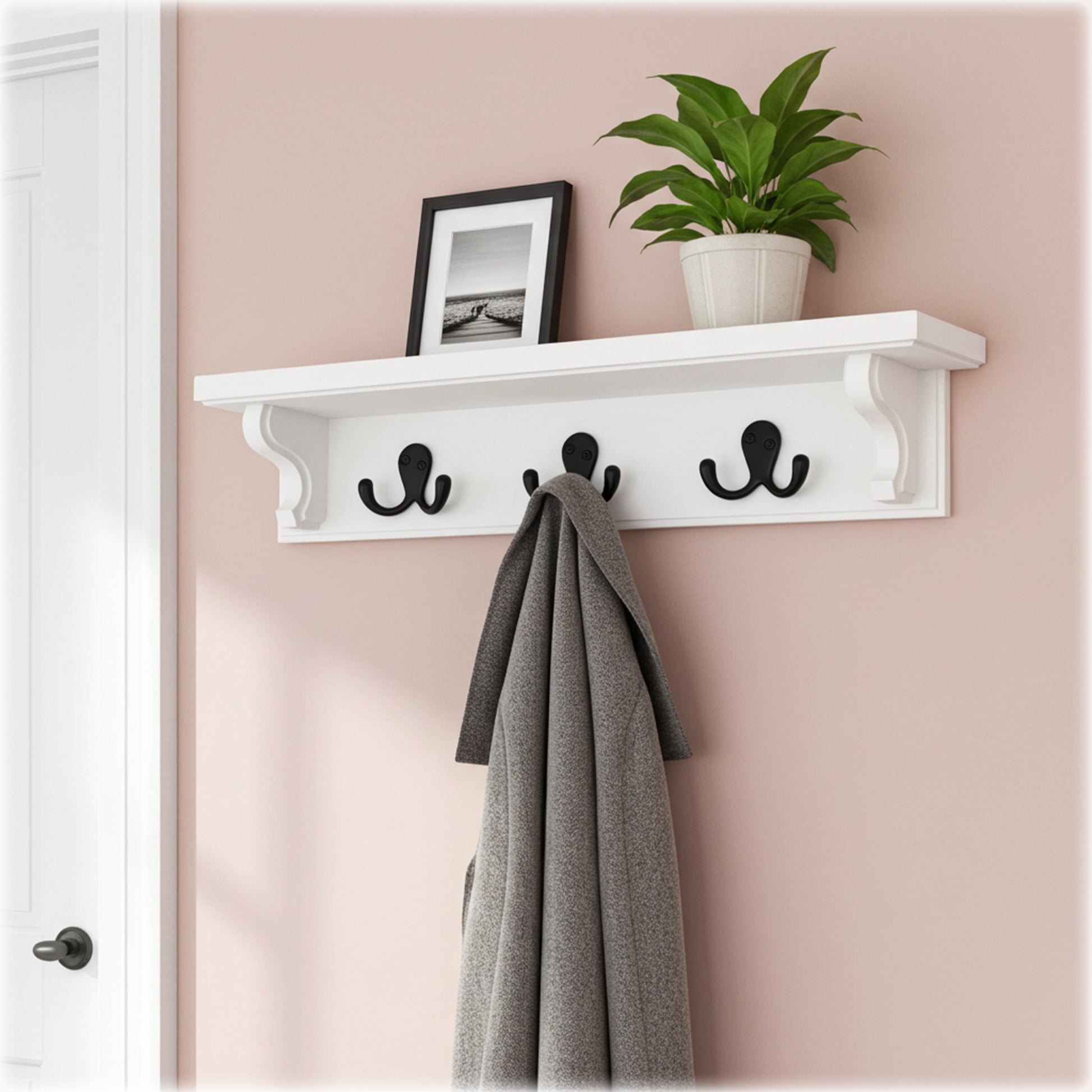 White wall shelf with hooks holding a coat and a plant against a pink wall.